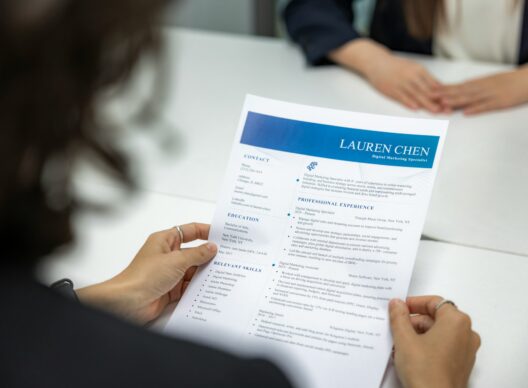 Deux mains tiennent un CV intitulé 'LAUREN CHEN Digital Marketing Specialist' affichant les sections Contact, Education, Relevant Skills et Professional Experience