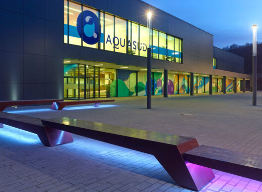 Façade du centre aquatique Aquasud le soir, grandes baies vitrées avec le logo 