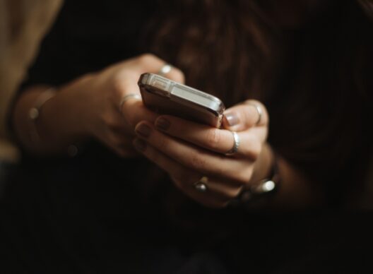 Plan rapproché de mains féminines ornées de bagues tapant un message sur un smartphone avec coque transparente