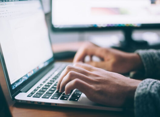 Mains tapant sur le clavier d’un ordinateur portable avec, à l’écran, un document Google Docs vide intitulé ‘ohne Vorlage - Google Docs’, le menu d’édition en allemand visible en arrière-plan.